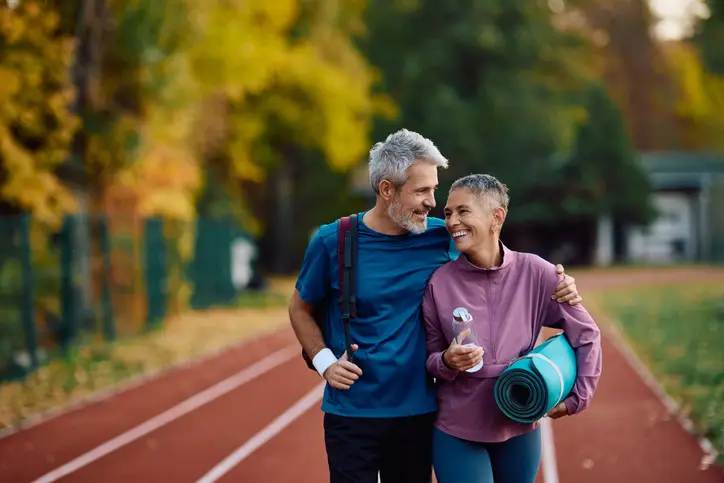 Happy mature athletic couple talking while going on sports training at the park.